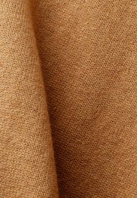 Gros plan d'un tissu tricoté doux marron avec une texture fine et régulière et des ombres subtiles mettant en valeur les plis.