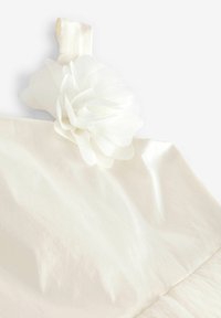 Biely látkový materiál s hladkou štruktúrou, zdobený viacvrstvovou kvetinovou aplikáciou v ľavom hornom rohu. Dizajn je jemne elegantný a jednoduchý.