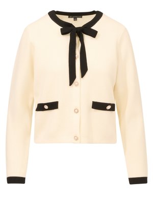 Cardigan crema con bordi neri, presenta un papillon al collo, due tasche anteriori e bottoni decorativi con un accento simile a una perla.