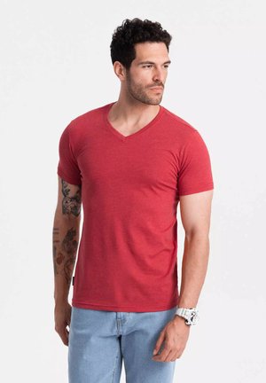 Camiseta de algodón roja con cuello en V y mangas cortas, diseño ajustado y textura suave. Combinada con jeans de mezclilla azul claro y un reloj blanco.