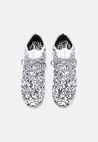 Scarpe sportive a motivi bianco e nero con un design texturizzato, lacci tradizionali e un interno imbottito con una fodera a stampa geometrica.