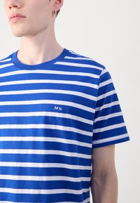 Sinine ja valge triibuline t-särk, mis on valmistatud puuvillast, ümmarguse kaeluse ja väikese "MN" logoga rinnal. Lühikesed varrukad ja vaba lõige.