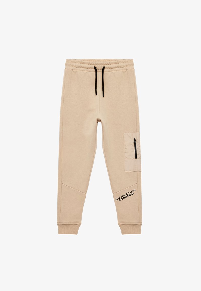 Beige sweatpants med snor i taljen, elastiske manchetter, sidelomme med lynlås og sort tekstdetalje langs benet. Blød tekstur.