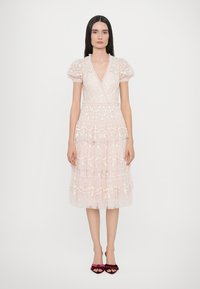 Lichtroze jurk met pofmouwen, gelaagd ontwerp, bloemendessin en een getailleerde taille. Versierd met delicate kantdetails.