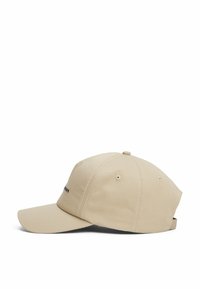 Beige cap with a curved brim, stitched detailing, and an adjustable strap at the back. Features small text on the front.
