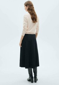 Sweter dziany w jasnoróżowym kolorze z dopasowanym stanem, zestawiony z długą, ciemną, plisowaną spódnicą oraz czarnymi, wysokimi botkami na obcasie, widok z tyłu.