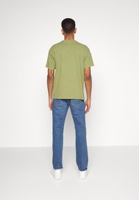 Camiseta de algodón verde oliva, de mangas cortas, corte relajado, combinada con jeans de denim azul claro, de corte recto, llevada con zapatillas blancas.