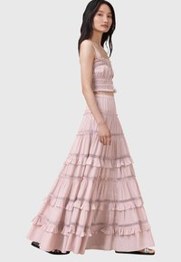 Falda larga de capas en color rosa con volantes y adornos de encaje, combinada con un top corto de smock a juego, que cuenta con tirantes finos.