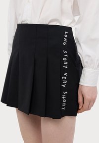 Mustikka hame, jossa valkoisella brodeeratun tekstin "LYHYESTI KOVASTI KERTOEN" sivussa. Valmistettu sileää tekstiiliä.