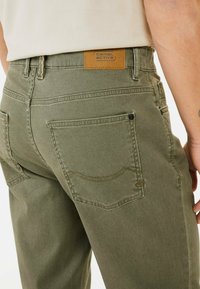 Olijfgroene katoenen broek met een beige leren label, voorzien van twee achterzakken met gestikte accenten en een rechte pasvorm.