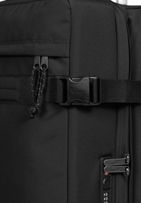 Valigia nera in tessuto caratterizzata da un design robusto, doppi zip con tiranti in corda, una chiusura a fibbia sicura e un dettaglio con lucchetto a combinazione.