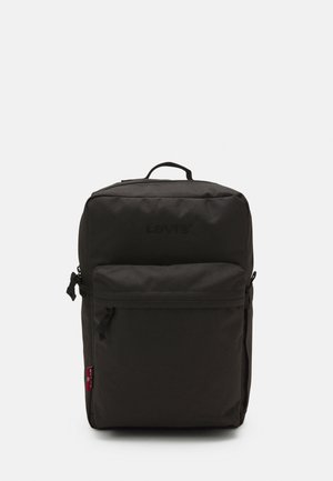 Sac à dos en tissu noir avec une poche zippée à l'avant, une poignée supérieure et un détail de logo. Texture lisse et forme rectangulaire. Fermeture zippée.