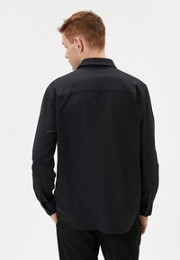 Camisa negra de manga larga hecha de una tela suave, con collar puntiagudo, puños de botón y un dobladillo recto en la parte posterior.