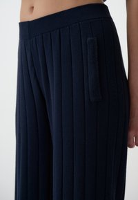 Marineblauwe, geribbelde wijde broek met een zachte textuur, voorzien van een brede tailleband en een zijzakdetail.