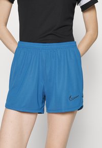 Siniset urheilushortsit, joissa on joustava vyötärö, mustalla Nike-swoosh-logolla ja sileä, kevyestä kankaasta valmistettu materiaali.