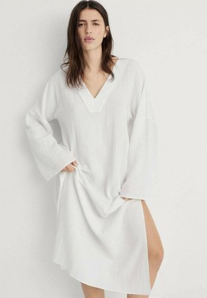 Robes blanches amples avec un décolleté en V profond et des manches longues. Le tissu texturé avec une fente sur le côté ajoute un intérêt visuel et facilite les mouvements.