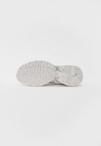 Bílá podrážka sportovní obuvi s texturovaným gumovým vzorem a strategicky umístěnými drážkami pro lepší trakci. Lehký design s kompaktním tvarem.