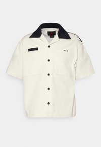 Camicia bianca a maniche corte con colletto blu navy, due tasche anteriori, chiusura a bottoni neri e un'etichetta con la scritta "No. 8" e dettagli del marchio.