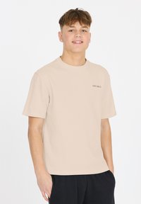 Beige bomuld t-shirt med rund halsudskæring og korte ærmer. Har et lille sort teksttryk "LES' ARCS" på venstre bryst.
