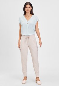 Lichtblauwe blouse met korte mouwen en V-hals, voorzien van drie knopen, gecombineerd met beige cargo-broek met trekkoord en lichte wedges.
