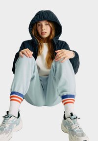 Kurtka z kapturem w kolorze granatowym, biała koszula, jasnoniebieskie dresy oraz trampki z siateczkowymi detalami. Kolorowe, paskowane skarpetki sięgające kostek.