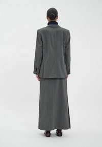 Veste de costume rayée grise et jupe longue en tissu texturé. Comprend une fente à l'arrière de la jupe et des chaussures noires.