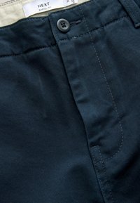 Navy blue barrel fit trousers made of cotton. Features a button closure, visible stitching, and a smooth texture with diagonal weave pattern.