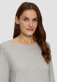 Lichtgrijze trui met een wijde halslijn en lange mouwen, gemaakt van een zachte stof met een gladde textuur. Subtiel, egaal ontwerp.