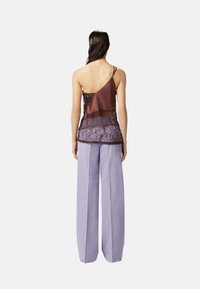 Top asimmetrico in raso marrone e pizzo abbinato a pantaloni larghi di un leggero lavanda. Il top presenta un bordo in pizzo e dettagli intricati.