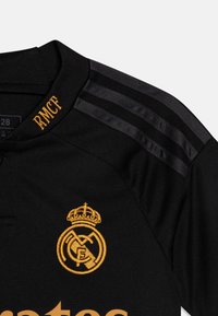 Musta urheilu paita, jossa on oranssit brodeeratut logot ja yksityiskohdat, pyöreä kaulus ja kolme teksturoitua raitaa hartioilla.