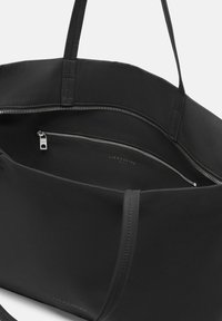 Czarna torba typu tote wykonana z gładkiego, trwałego materiału, z zamykaną komorą, prostym wnętrzem i dwoma solidnymi uchwytami. Posiada dyskretną markę.