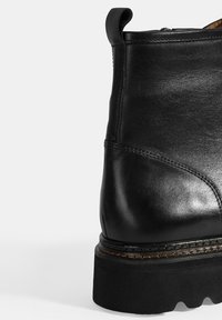 Zwarte leren enkelboot met een gladde textuur, ronde neus, stevige platformzool en een trekband aan de achterkant voor gemakkelijk aan- en uittrekken.