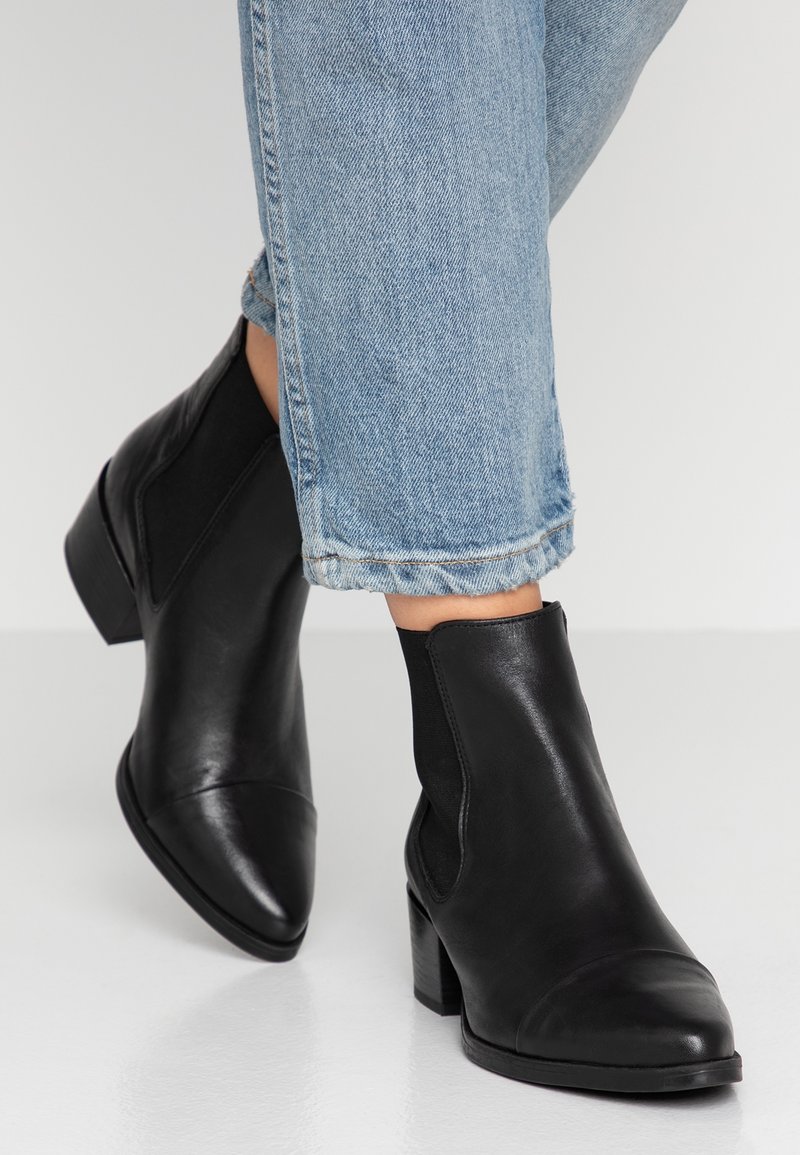 Stivaletti neri in pelle con punta a punta, pannelli laterali elasticizzati e tacco spesso, abbinati a jeans di denim azzurro chiaro arrotolati.