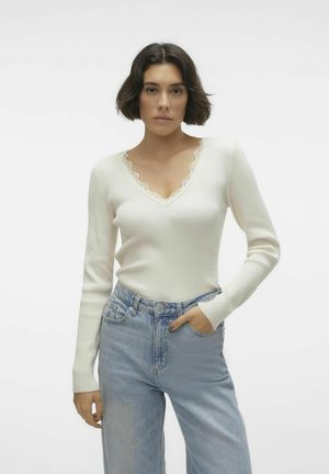Haut à manches longues blanc à côtes avec un décolleté en V festonné et une coupe ajustée, associé à un jean taille haute bleu clair.