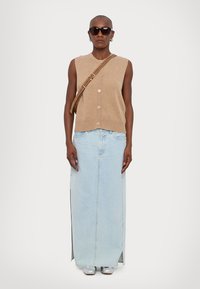 Beige strikket vest med knapper, kombinert med en lyseblå denim maxi-skjørt med sidelommer, og sølvfargede sko. Tilbehør: brun skulderveske.