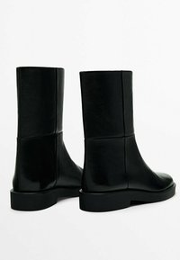 Black ankle boots made of textured leather with a sleek, minimal design. Features a flat, solid black sole and no visible hardware.