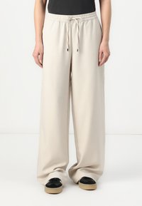 Wide-leg, lightweight trousers in a light beige fabric with an elastic waistband and adjustable drawstring, featuring side seam details.