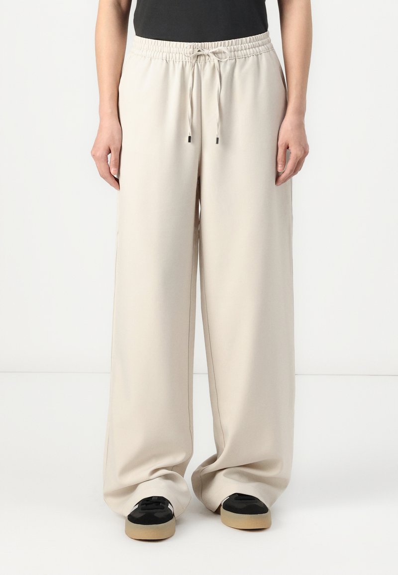 Wide-leg, lightweight trousers in a light beige fabric with an elastic waistband and adjustable drawstring, featuring side seam details.