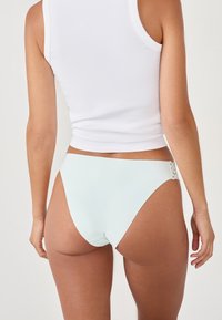 Bas de bikini bleu clair avec un design taille haute, texture sans couture, et accent en dentelle sur le côté. Le matériau semble lisse et extensible.