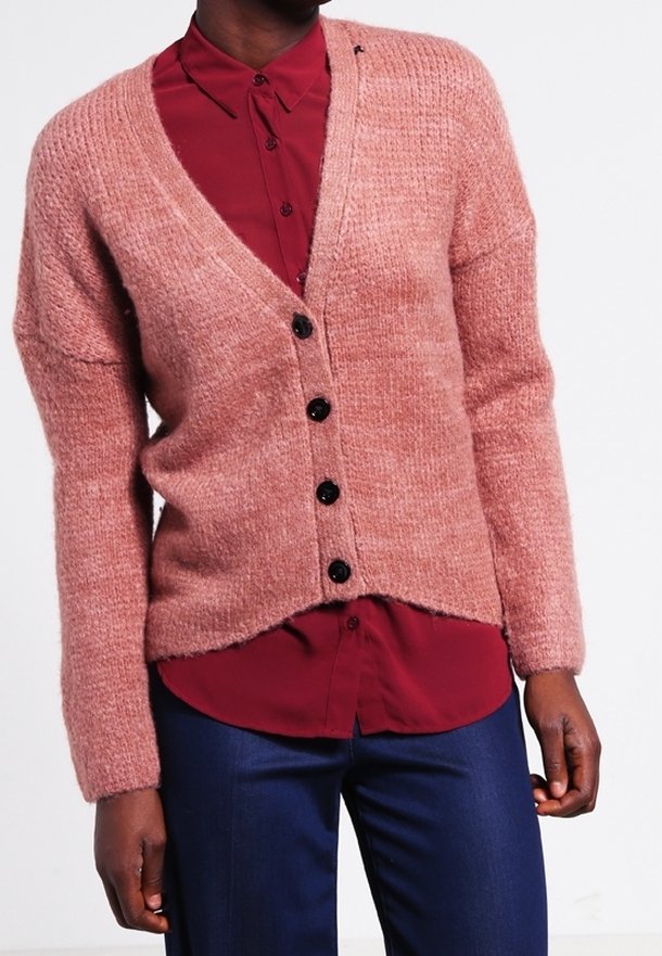 Lyserød strikket cardigan med V-hals, ribbet struktur og sorte knapper. Kombineret med en mørkerød skjorte med knapper under. Ingen synlige mønstre.