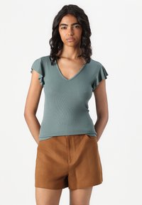 Teal ribbed short-sleeve top with a V-neck and ruffled sleeves, paired with brown suede shorts, both fitted and smooth texture.