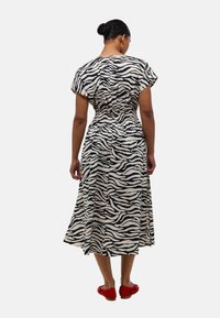 Robe midi rayée noir et blanc avec des manches courtes, taille élastiquée et jupe fluide, assortie à des ballerines rouges.