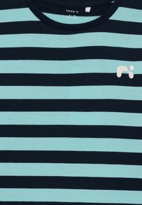 Stribet t-shirt i lys blå og marineblå stof. Har en rund hals og lille broderet logo på venstre bryst.