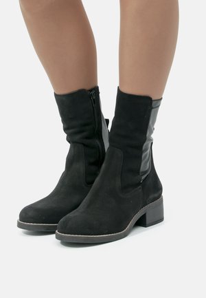 Botas de tobillo de ante negro con cierre de cremallera y acento de cuero negro. Tacón cuadrado y acabado texturizado. Diseño clásico adecuado para el uso diario.