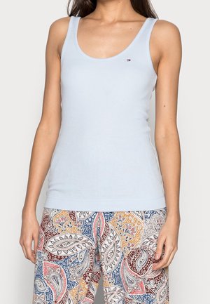 Mujer vistiendo una camiseta sin mangas azul claro y pantalones con un patrón de cachemir multicolor, posando frente a un fondo liso.