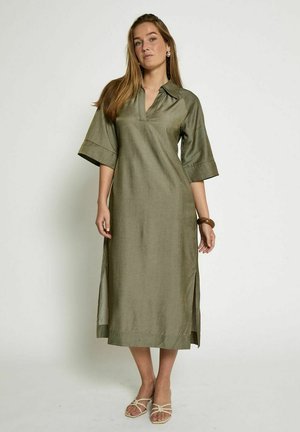 Olive green, linen dress with a collared neckline, short wide sleeves, side slits, and a long, straight silhouette. Worn with minimalistic sandals.
