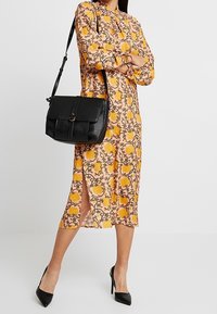 Abito a fantasia floreale in pesca con accenti gialli, caratterizzato da maniche lunghe e spacchi laterali; abbinato a una borsa a tracolla nera in pelle strutturata.