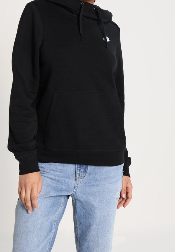 Svart hoodie gjord av mjukt tyg med en känguruficka, snodd i huvan och en liten logotyp på bröstet, ihop med ljusblåjeans.