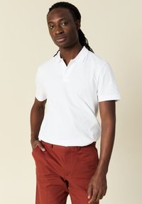 Wit polo shirt met korte mouwen, een kraag en een sluiting met drie knopen, gecombineerd met roestkleurige broek, gladde stof, relaxte pasvorm.