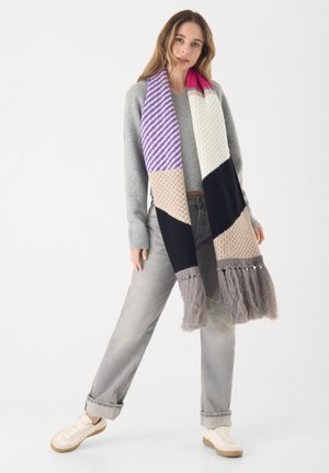 Écharpe tricotée multicolore avec des rayures, des motifs texturés et des franges. Les couleurs incluent le violet, le blanc, le noir, le beige et le gris.